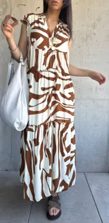 Vestido largo color blanco con estampado abstracto en marrón, con escote en V y corte escalonado.