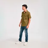 Camisa de manga corta color verde oliva con dos bolsillos de parche en el pecho con cierre de solapa y botón. Logo de Caterpillar bordado en la solapa del bolsillo izquierdo. Corte recto y cierre frontal con botones.