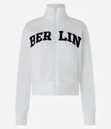 Chaqueta deportiva blanca con cierre frontal, cuello alto y puños ajustados. Presenta la inscripción "BERLIN" en letras negras y gruesas en el pecho.