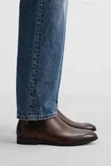 Bota Chelsea de cuero color marrón oscuro, con puntera fina, paneles laterales elásticos y tirador trasero.