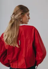 Campera bomber color beige de cuero, con cuello redondo, cierre frontal con botones a presión, mangas largas con puños elásticos y detalles de tachas metálicas en hombros y espalda.