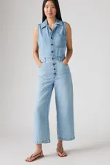 Mono de jean celeste claro, sin mangas, con cuello camisero, cierre frontal con botones y bolsillos laterales.