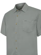 Camisa de manga corta color beige, con cuello clásico, cierre frontal con botones y bolsillo en el pecho izquierdo.