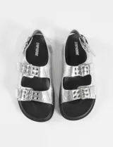 Sandalias plateadas con tiras anchas y plantilla cómoda, con tira ajustable en el talón. Fabricadas en cuero vegano.