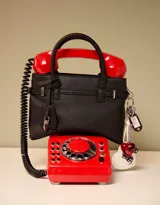 Cartera tipo city de cuerina color negro con correa con charm decorativo, manijas superiores con abrojo y cierre superior.