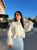 Blusa color blanco hueso, de cuello alto con volados, mangas largas acampanadas con volados y corte crop.