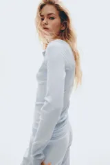 Remera ajustada de punto acanalado suave, color celeste, con manga larga, cuello redondo ribeteado en picot y tapeta de botones.