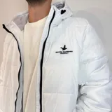 Campera inflada color ocre con capucha, cierre frontal con cremallera y logo de la marca bordado en el pecho.