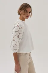 Blusa blanca de mangas 3/4 con bordado calado y cuello redondo con volados.