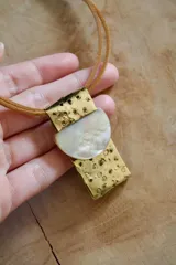 Collar con cordón de cuero marrón, dije de bronce con perforaciones y aplique de nácar en forma de media luna.