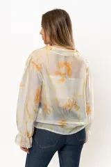 Blusa blanca traslúcida con estampado floral color naranja, cuello con volados y mangas largas abullonadas con puños elásticos.