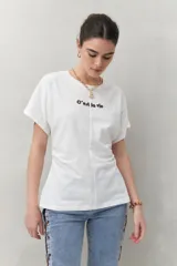 Remera blanca de manga corta con bordado frontal "C’est la vie", calce relajado y frunces laterales.