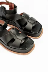 Sandalias negras de cuero con plataforma y tiras cruzadas en el empeine y tira con hebilla alrededor del tobillo.