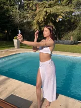 Conjunto de bikini blanco tejido a crochet, compuesto por un top triangular con volados y una pollera larga calada con cordón ajustable en la cintura.