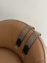 Cinturón negro de cuero ecológico con hebilla dorada y múltiples ojales dorados.