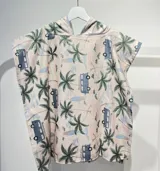 Poncho toalla con capucha, estampado con diseño de hojas y mariposas en tonos rosa, naranja y gris sobre fondo celeste.