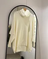 Polerón color crudo de corte oversize, con cuello drapeado y mangas largas caídas. La parte delantera es más corta que la trasera.