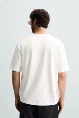 Camiseta blanca de corte holgado, cuello redondo y mangas cortas. Presenta un bordado y estampado combinado en el frente.