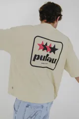 Remera color beige de corte holgado, con cuello redondo y mangas cortas. Estampado pequeño en el pecho con el logo de la marca Pulau.