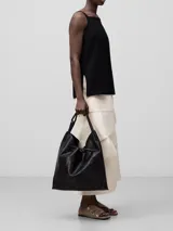 Bolso maxi hobo negro de piel bovina, con cantos al taglio, puntadas gruesas, un compartimento, cierre con nudo, asa de hombro y logo grabado.