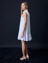 Vestido corto blanco de gasa, sin mangas, con cuello camisero, abertura central con botones y terminación de ruedo con volado.