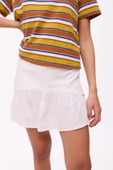 Falda corta blanca de lino con textura, de corte evasé y un volante fruncido en el ruedo.