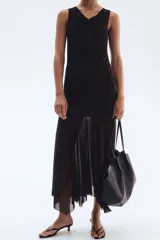 Vestido largo hasta el tobillo, sin mangas, en malla con estampado de leopardo en tonos oscuros. Presenta un escote drapeado tipo cascada, frunces laterales y una falda acampanada con bajo asimétrico y deshilachado.