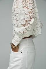 Top de encaje blanco con cuello redondo, mangas largas abullonadas y puños con botones metálicos.