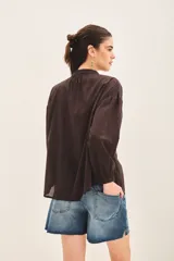 Camisa blanca de voilé de algodón con escote redondo y bordados de ojos en el delantero. De corte recto y mangas largas con puños abotonados.