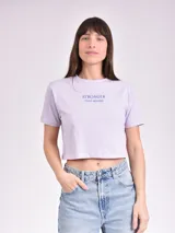 Remera corta color lila con estampado frontal con la frase "Stronger than before" en azul.