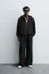Sudadera negra con capucha, corte boxy, cierre frontal con cremallera, bolsillos laterales y puños elásticos.