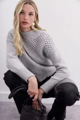 Polera de cuello bajo, tejida en hilado gris mélange suave al tacto, con pompones en la pechera y hombros.