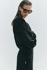 Blusa negra semitransparente con escote en pico, cordón ajustable y mangas largas con elástico en los puños.