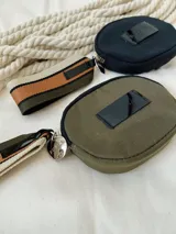 Monedero negro circular con cierre de cremallera y llavero de cinta estampada a rayas.