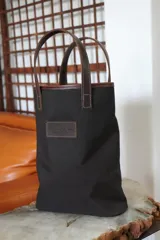 Bolso matero de lona color azul con detalles en cuero marrón, con asas cortas y logo de la marca en cuero.