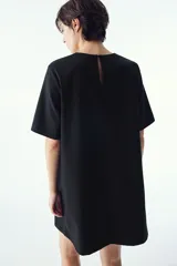 Vestido corto negro con cuello redondo y abertura de cerradura con botón oculto en la nuca. Modelo de manga corta con pinzas en el busto y bajo recto.