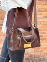 Cartera bandolera de cuero color marrón chocolate, con forro de tela y herrajes dorados. Tiene doble asa de mano y correa larga regulable y desmontable. Incluye bolsillo frontal con cierre y bolsillo interno.