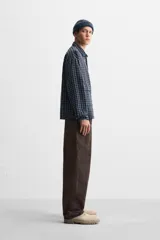 Camisa de hombre a cuadros azules y negros, de corte cuadrado, con cuello solapa, manga larga con puños abotonados, cierre frontal con botones y bolsillos de parche con solapa en el pecho.