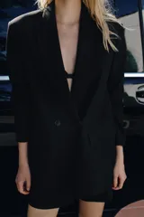 Blazer negra oversize con cuello solapa, manga larga con hombreras, bolsillos delanteros con solapa y cierre frontal cruzado con botones.