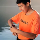 Remera deportiva naranja de poliéster y spandex, con logo Merrell estampado en el pecho.