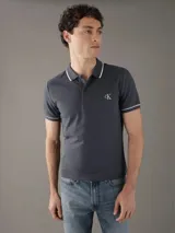 Chomba Calvin Klein color gris con cuello polo, tapeta de dos botones, logo bordado en el pecho y ribetes blancos en cuello y mangas. Corte slim fit.