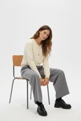 Cardigan acrílico color natural, de corte ajustado, con cuello redondo y botones frontales.