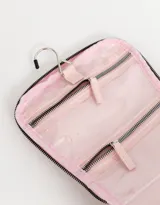 Neceser de viaje color rosa con cierre superior y manija. Estampado frontal con un moño rojo con corazones y la frase "Très Chic".