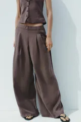 Pantalón palazzo color marrón topo, de tejido fluido, tiro medio, cintura elástica, bolsillos laterales y pinzas frontales.
