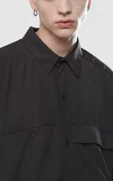 Camisa negra de manga corta con doble bolsillo ojal en delantero, realizada en tejido plano y silueta oversize.