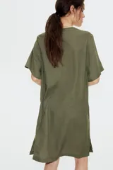 Vestido túnica a la rodilla en tejido liviano de viscosa color verde oliva con cuello mao y abertura en V. Modelo de corte holgado con hombros levemente caídos, mangas cortas y bajo recto con tajos laterales.
