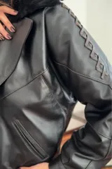 Campera bomber negra de cuero con cuello de piel sintética, forro interior y detalles de pasamanería en cuero marrón gastado.