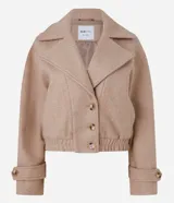 Saco bomber corto color beige confeccionado en polivelour, con cuello virada, solapa, cierre con botones delanteros y elástico en la cintura.