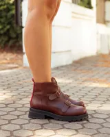 Botinetas de cuero color marrón con suela track negra. Presentan un cierre frontal con detalle en color rojo, dos correas con hebillas metálicas ajustables y puntera redondeada.