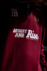 Buzo de algodón color bordó, estilo universitario, con cierre medio frontal y cuello alto. Estampado frontal con el texto "Since 19" y un ancla con laureles en amarillo y blanco.